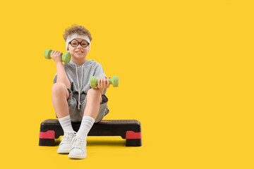 Sporty little boy exercising with dumbbells on aerobic stepper against yellow background