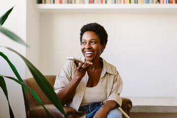 Mature Brazilian woman smiling while talking on smartphone in living room