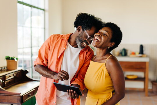Happy mature couple laughing and enjoying themselves with a tablet at home