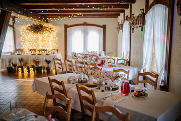 Elegant rustic dining hall set for an event with wooden chairs, white linens, floral decor, and warm fairy lights ambiance..