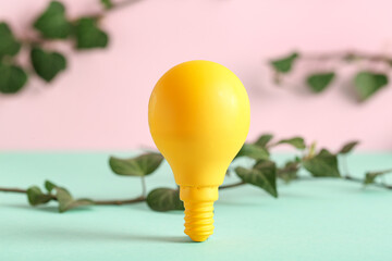 Yellow light bulb with leaves on color background. Concept of green technology