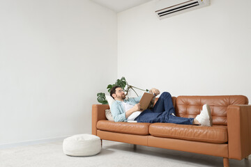Handsome man reading magazine with air conditioner in living room