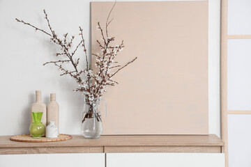 Vase with blooming tree branches on chest of drawers in stylish room, closeup