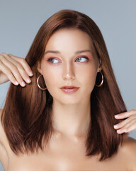 Fototapeta premium Studio shot of stylish redhead woman with glowing skin and hoop earrings, gently touching her shiny hair. Ideal for beauty, hair treatment, and fashion-themed advertisements or banners.