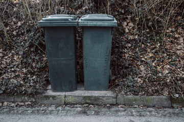 Fototapeta premium Two black garbage bins placed on the street near a house, creating a typical urban scene. A simple yet practical image showcasing everyday life and waste management in a residential area