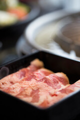close-up image features several strips of raw beef neatly arranged in a black container at korean hotpot restaurant , showcasing the rich, marbled texture of the meat with its deep red and white hues.