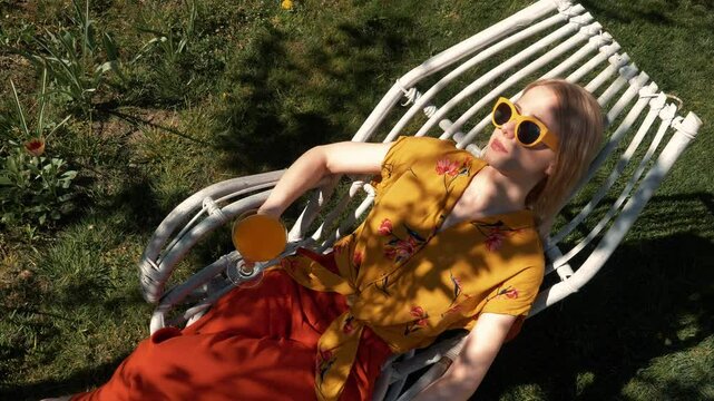 Blonde European woman relaxing with cocktail under tree shade in spring
