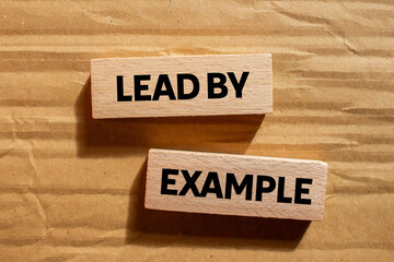 Lead by example message written on wooden blocks on cardboard background. Conceptual lead by...