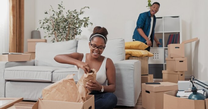 A girl in her freshly renovated flat unpacks cardboard boxes. She discovers an old photo, touches it gently, and calls her partner with a joyful smile on her face.