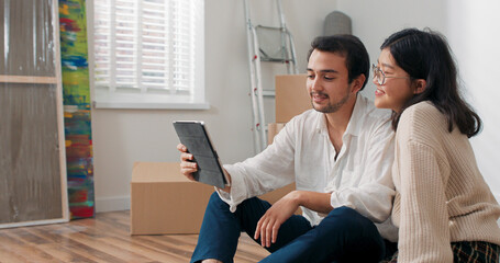 In a bright room, a couple sits on the floor. They wave to the tablet screen, chatting with parents and celebrating their move into a new apartment.