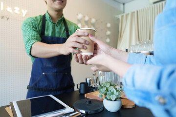 Sustainability and Enjoying Coffee. A barista hands a customer a coffee in a sustainable cup, emphasizing eco-conscious consumption.