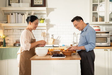 Asian senior couple cooking breakfast in the kitchen. husband helping wife on the morning weekend. Retired people enjoying lifestyle at the preparing counter