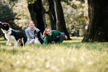 Two women teenagers walking with dogs in nature. They laugh, dogs run and play. Sunny day in the forest.
