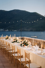 Bouquets of flowers stand on a long festive table on a terrace by the sea