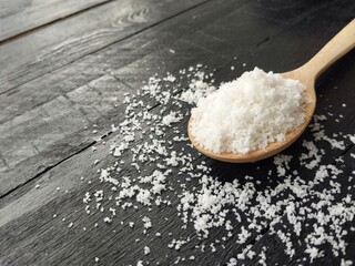 Pile of salt on wooden spoon with black wooden table background. Food ingredient, high angle view 