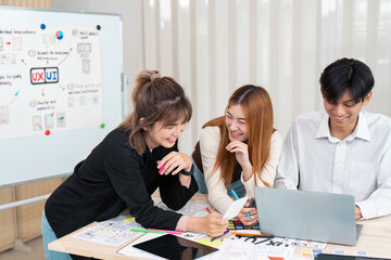 Engaged Design Team and Creative Ideas. Three designers share laughter and brainstorm during a vibrant UX UI project meeting.