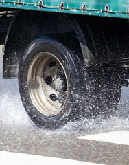 A truck is driving down a wet road with water spraying out from the back