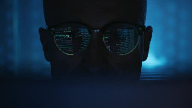 Male scientist working on a computer in a futuristic research laboratory. Computer screen displaying lines of code reflecting in glasses