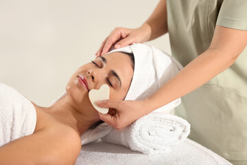 Young woman receiving facial massage with gua sha tool in spa salon