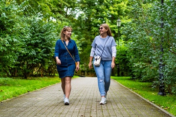 Obraz premium Two happy mature women walking in city park. Meeting of friends in park. Front view