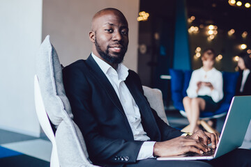 Portrait of experienced male entrepreneur in formal suit sitting in office chair and looking at...