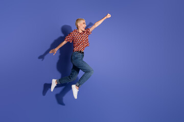 Obraz premium Young stylish woman joyfully jumping in mid-air wearing trendy casual clothes on violet background