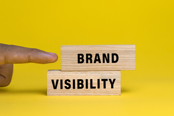 male finger pointing brand visibility words text on wooden blocks isolated on yellow background