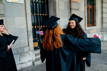 Group of students joyfully hugging and celebrating graduation day in front of their university,...