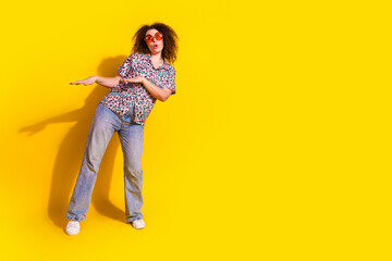Young woman with curly hair in casual attire posing joyfully against a vibrant yellow background making a playful gesture