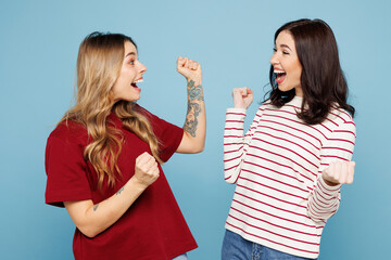 Young happy couple two friends women wears red casual clothes together do winner gesture celebrate clenching fists say yes isolated on pastel plain light blue cyan background studio Lifestyle concept