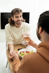 A happy gay couple holding hands and toasting with wine at lunch time