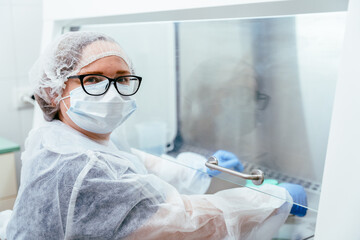 Female technician looking through lab window in protective gear