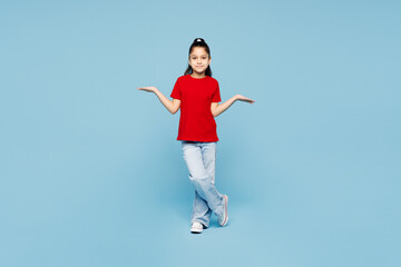 Fototapeta premium Full body little kid girl 8-9 years old wears red t-shirt have fun shrugging shoulders spread hands isolated on blue color background child studio portrait. Mother's Day love family lifestyle concept.