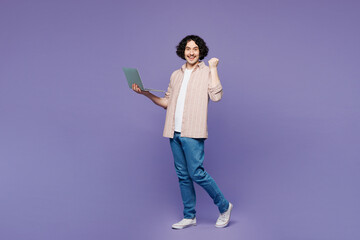Full body young IT man wear pink shirt t-shirt casual clothes hold use work on laptop pc computer do winner gesture isolated on plain pastel light purple background studio portrait. Lifestyle concept