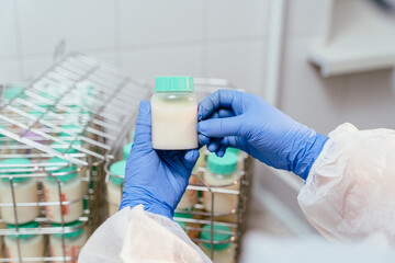 Top view of hands holding milk container above full storage baskets in breast milk lab - obrazy, fototapety, plakaty