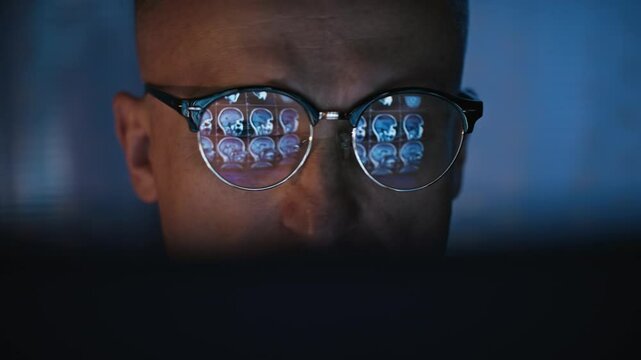 Male scientist working on a computer in a futuristic research laboratory. computer screen displaying MRI scan results reflecting in glasses
