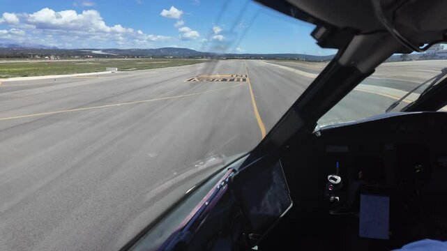 An immersive pilot FPV POV taken from a jet cockpit taxiing along an airpoprt taxiway, in a sunny day with a blue sky with few clouds.