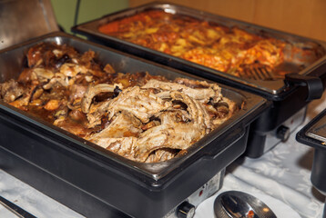 Buffet style tray with cooked pork ribs and cheesy potato casserole at catered event