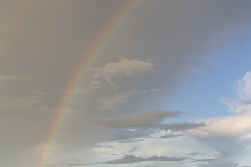 Thin rainbow on cloudy sky.