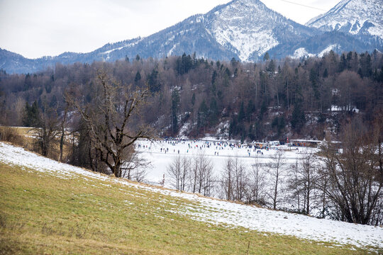 Winter wonderland: people ice skating on frozen lake with snowy mountain backdrop