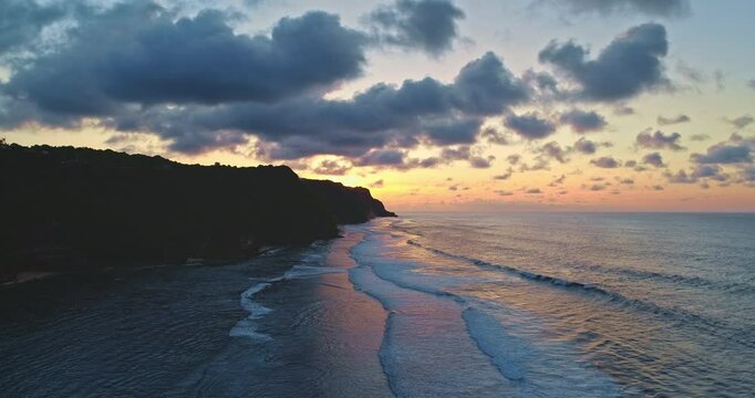Soft waves rolling gently toward the shore at sunset along the stunning Bali coast in Indonesia, with dramatic clouds enhancing the breathtaking scenic beauty of the landscape