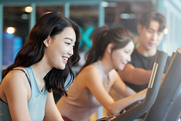 Young Asian Women and Man Exercising Together on Treadmills at Gym
