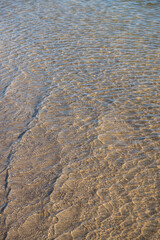 close view of water edge meeting sandy beach light reflections on the surface of shallow water