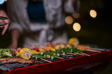 A woman is cooking food on a grill with a variety of vegetables and fruits