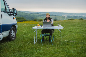 Freelancer working remotely on laptop near camper van in nature