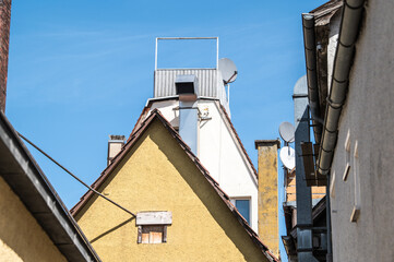 Hausgiebel mit Lüftungsrohren, Dachgarten, Kaminen und Satellitenschüsseln in verdichteter Bebauung  vor blauem Himmel in Reutlingen.