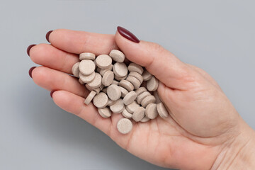 Cupped womans hand with a pile of beige medical pills top view over grey
