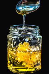 Macro details of honey flowing from a spoon into a glass jar