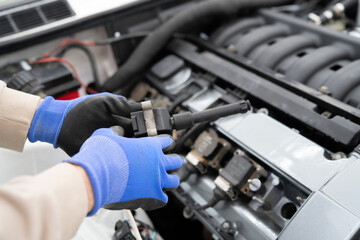 Fototapeta premium Car Mechanic Working With Ignition Coil in an Automotive Garage, Focused on Engine Repair