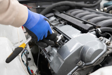 A mechanic in gloves using a wrench to tighten a spark plug in an engine during a vehicle repair session inside the workshop.